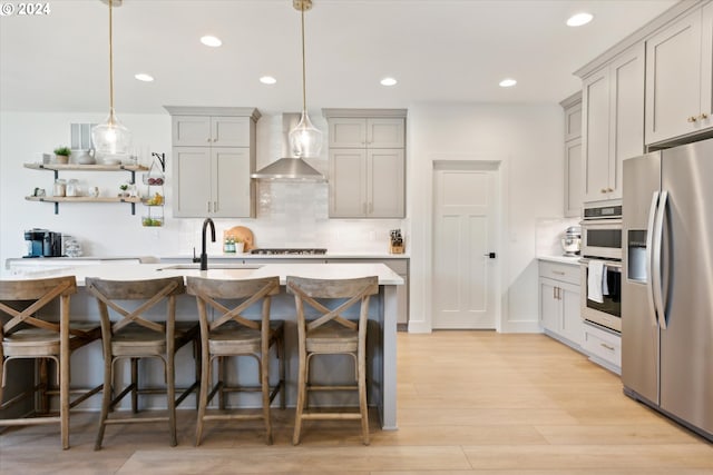 kitchen with wall chimney range hood, sink, decorative light fixtures, light wood-type flooring, and appliances with stainless steel finishes