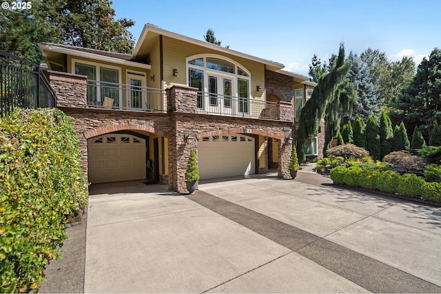 view of front of house featuring stone siding, french doors, concrete driveway, an attached garage, and a balcony