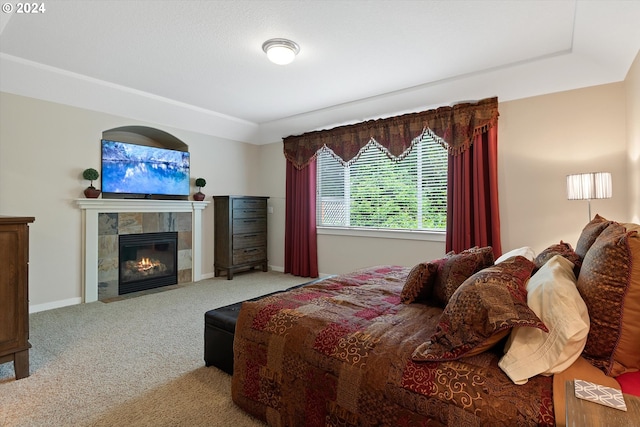 bedroom with light carpet, a tiled fireplace, and a raised ceiling