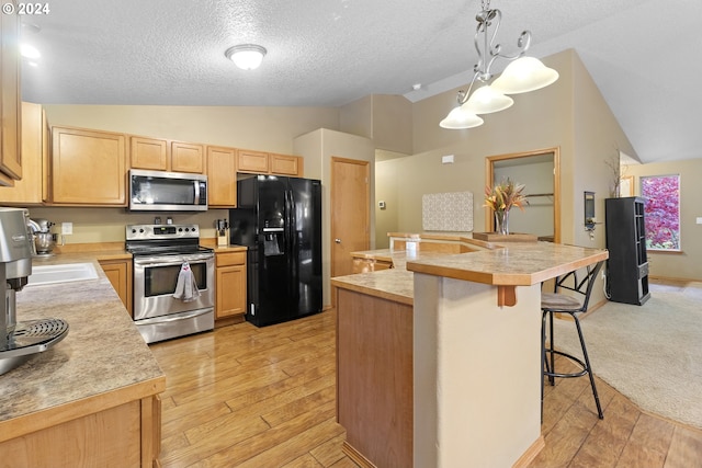 kitchen with vaulted ceiling, light wood-type flooring, appliances with stainless steel finishes, and decorative light fixtures