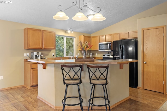 kitchen with light wood-type flooring, appliances with stainless steel finishes, a kitchen bar, hanging light fixtures, and lofted ceiling