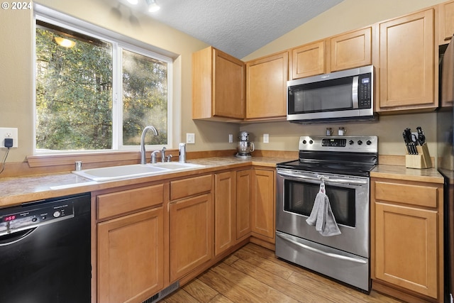 kitchen featuring sink, appliances with stainless steel finishes, a textured ceiling, lofted ceiling, and light wood-type flooring