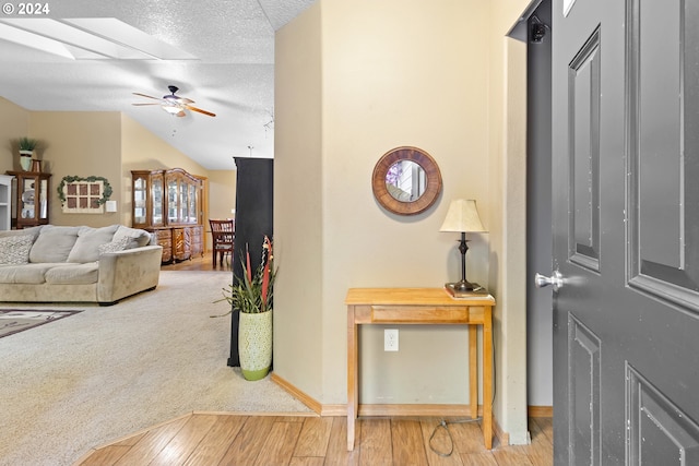 interior space with vaulted ceiling with skylight, a textured ceiling, hardwood / wood-style flooring, and ceiling fan