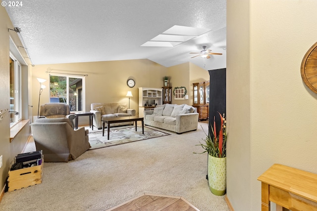 living room with vaulted ceiling with skylight, ceiling fan, a textured ceiling, and carpet floors