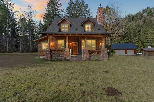 view of front of house featuring an outbuilding, covered porch, a chimney, and a front yard