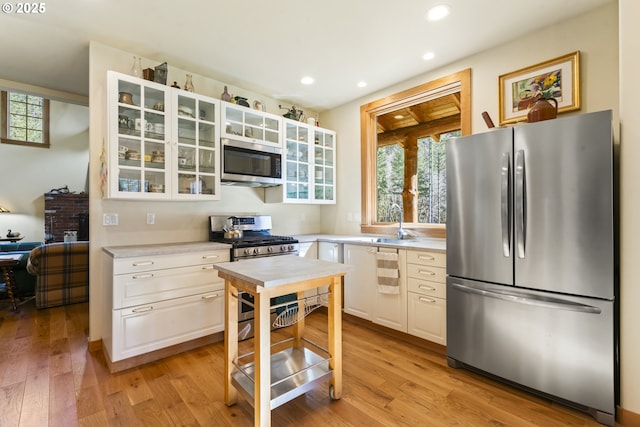 kitchen with glass insert cabinets, appliances with stainless steel finishes, light countertops, and light wood-style floors