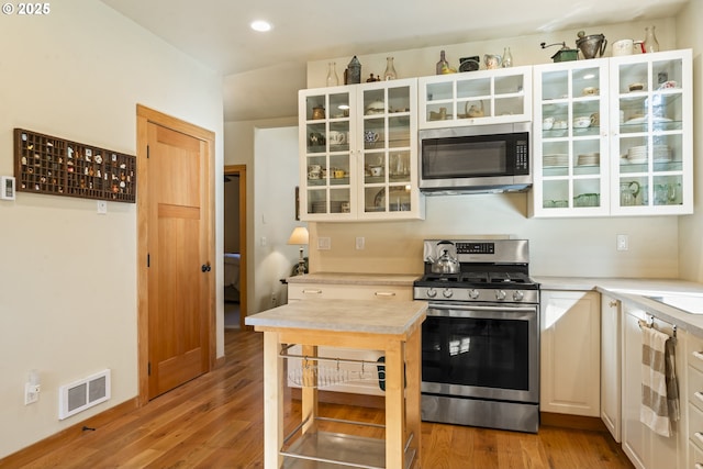 kitchen featuring visible vents, light wood finished floors, light countertops, glass insert cabinets, and appliances with stainless steel finishes