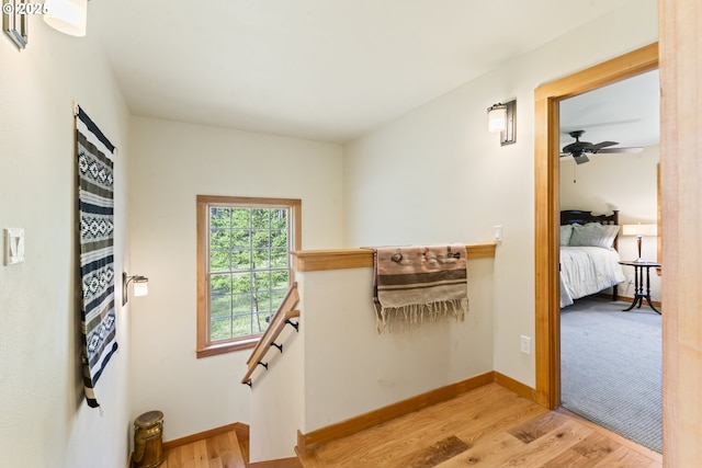 hallway featuring an upstairs landing, light wood-type flooring, and baseboards