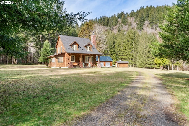 view of front of home featuring a chimney, driveway, a forest view, and a front lawn