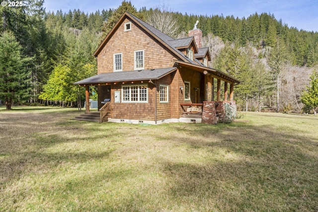 view of property exterior featuring a view of trees, a lawn, roof with shingles, and a chimney