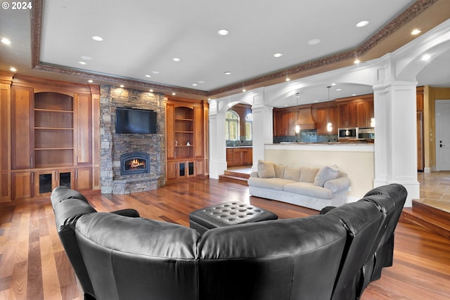 living room featuring light wood-type flooring, decorative columns, and a stone fireplace