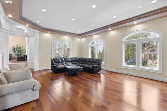 living room with a healthy amount of sunlight, dark hardwood / wood-style flooring, decorative columns, and a raised ceiling