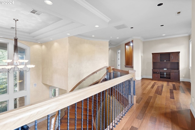 corridor with a tray ceiling, a notable chandelier, light hardwood / wood-style floors, and crown molding