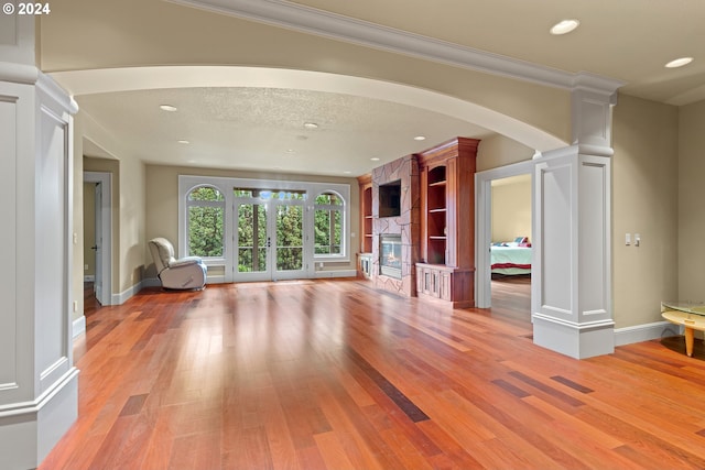 unfurnished living room with light hardwood / wood-style flooring, a fireplace, a textured ceiling, french doors, and ornate columns