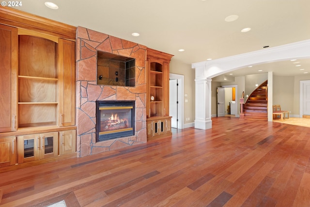 unfurnished living room featuring light hardwood / wood-style floors, a stone fireplace, ornate columns, and built in shelves