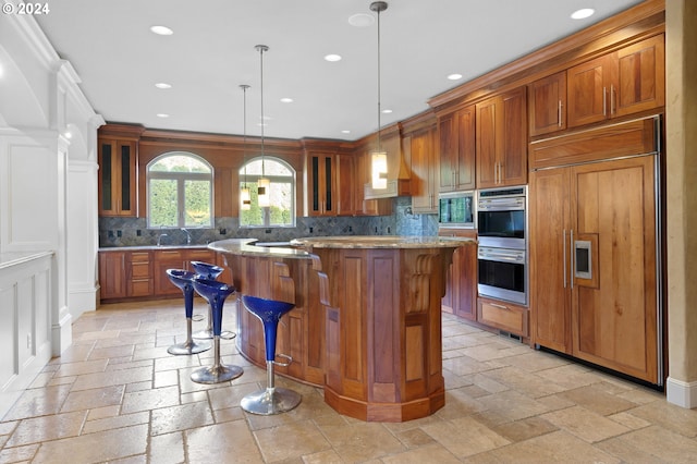 kitchen featuring built in appliances, a kitchen bar, premium range hood, backsplash, and hanging light fixtures