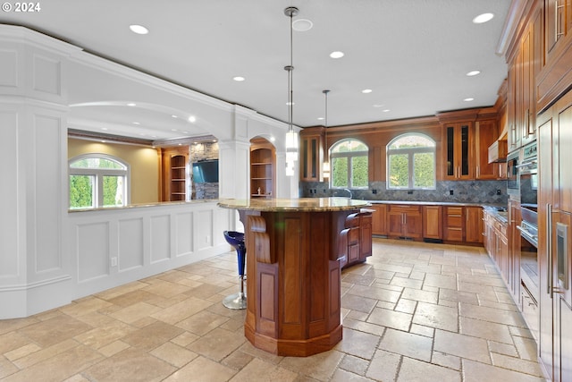 kitchen featuring backsplash, a breakfast bar area, dark stone counters, decorative light fixtures, and a healthy amount of sunlight