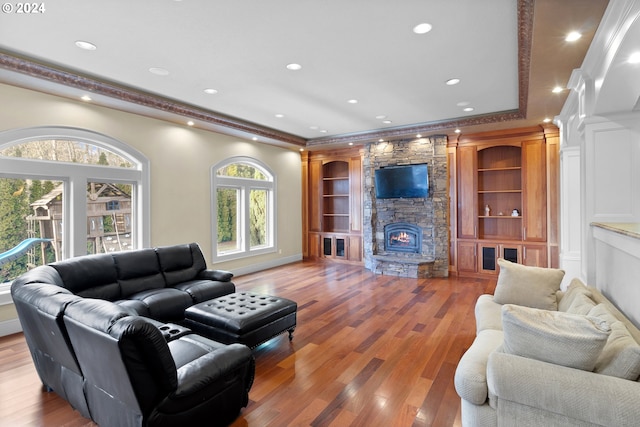 living room featuring built in shelves, crown molding, a fireplace, and hardwood / wood-style flooring