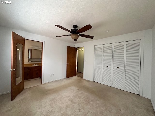 unfurnished bedroom featuring a closet, ceiling fan, connected bathroom, and light carpet