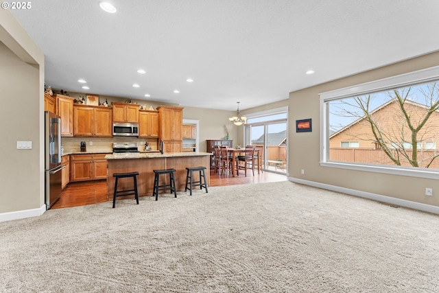 kitchen with appliances with stainless steel finishes, a kitchen island with sink, light stone countertops, a kitchen bar, and light colored carpet