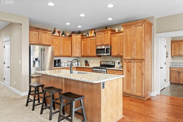 kitchen featuring sink, a breakfast bar, appliances with stainless steel finishes, a center island with sink, and decorative backsplash