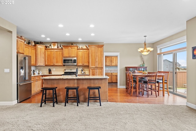 kitchen with hanging light fixtures, stainless steel appliances, a kitchen breakfast bar, a center island with sink, and light carpet