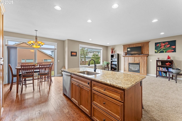 kitchen with sink, hanging light fixtures, light stone countertops, a center island with sink, and stainless steel dishwasher