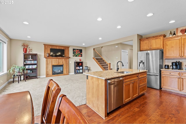 kitchen featuring sink, stainless steel appliances, light stone countertops, dark wood-type flooring, and a center island with sink