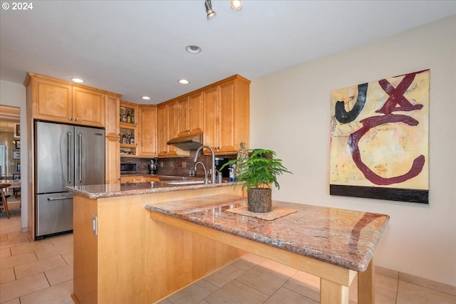 kitchen featuring high end fridge, light stone counters, kitchen peninsula, and tasteful backsplash