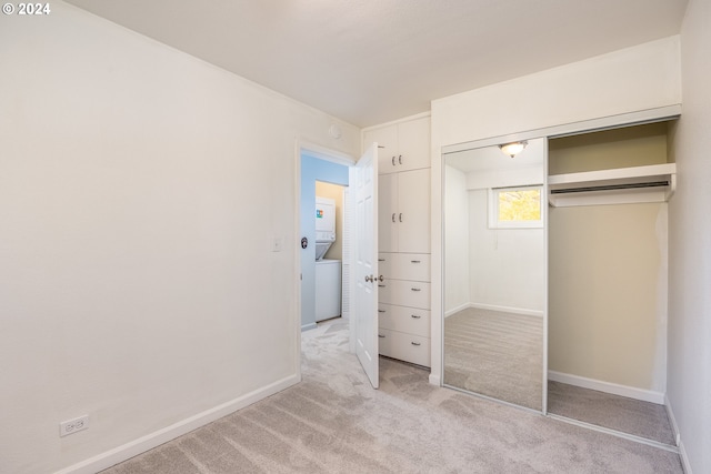 unfurnished bedroom featuring a closet, light colored carpet, and stacked washer / drying machine