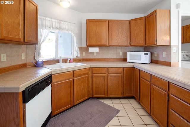 kitchen featuring tile countertops, white appliances, sink, light tile patterned floors, and tasteful backsplash