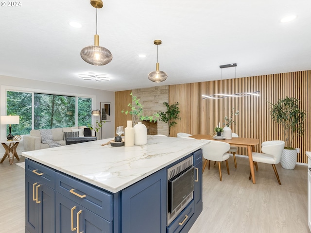 kitchen with stainless steel microwave, hanging light fixtures, light wood-type flooring, blue cabinets, and light stone counters