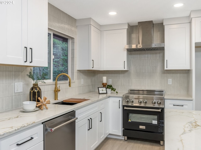 kitchen with sink, appliances with stainless steel finishes, wall chimney range hood, and white cabinetry