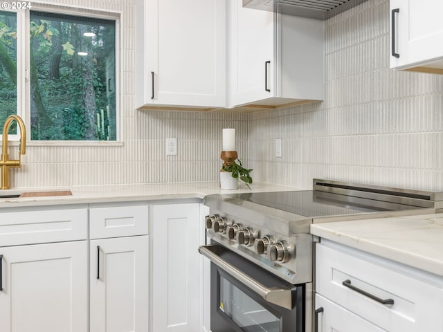 kitchen with backsplash, white cabinetry, light stone countertops, high end stainless steel range, and sink