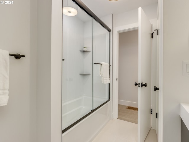 bathroom with wood-type flooring and bath / shower combo with glass door