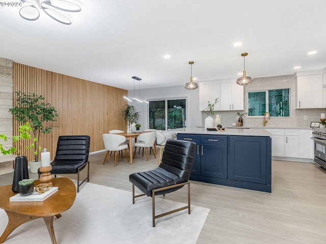 kitchen featuring decorative backsplash, light hardwood / wood-style flooring, pendant lighting, blue cabinetry, and wood walls