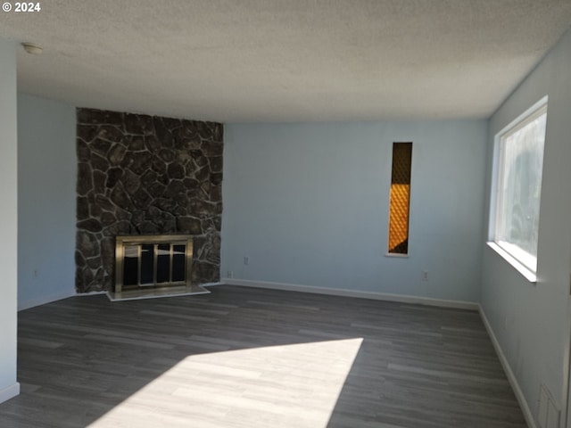 unfurnished living room with a stone fireplace, dark wood-type flooring, and a textured ceiling