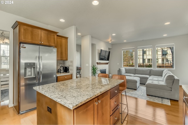 kitchen with light wood-style flooring, light stone counters, a kitchen island, stainless steel fridge, and brown cabinetry