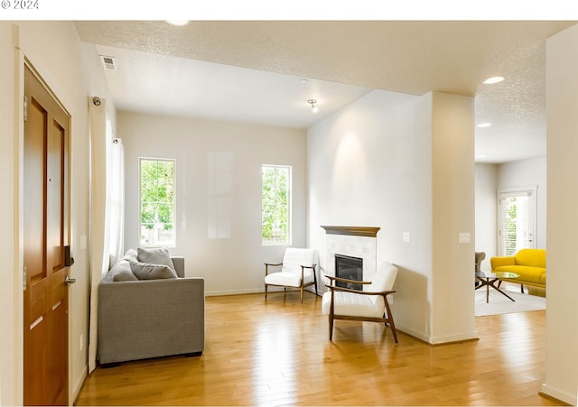 living area with visible vents, a textured ceiling, light wood-style floors, baseboards, and a tile fireplace