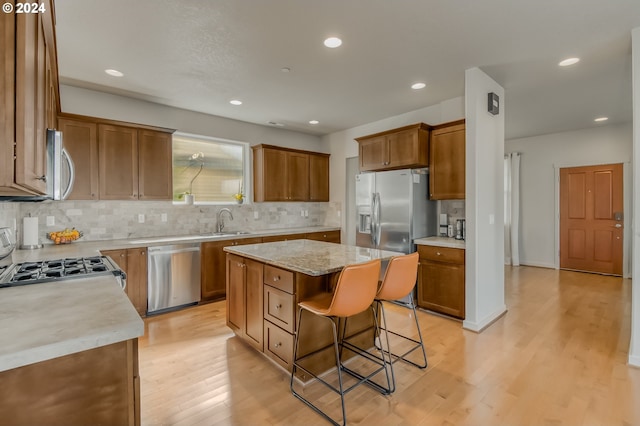 kitchen featuring light wood finished floors, a breakfast bar, a sink, stainless steel appliances, and backsplash