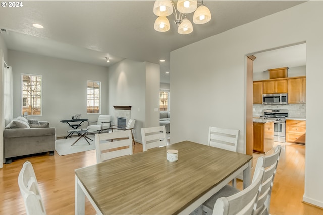 dining area featuring recessed lighting, a notable chandelier, light wood-style floors, and a glass covered fireplace