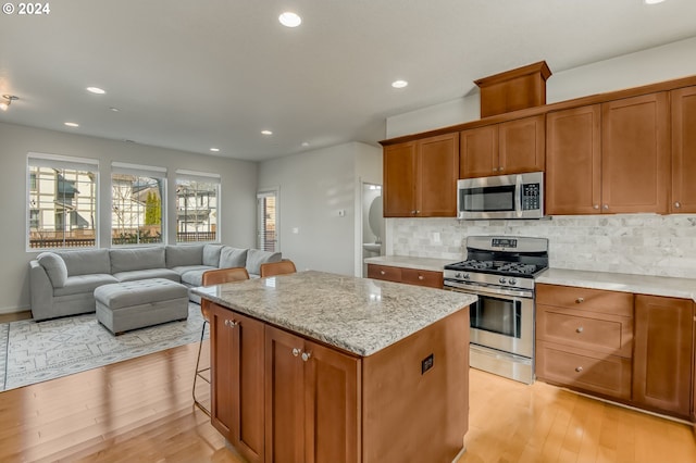 kitchen featuring light wood-style flooring, appliances with stainless steel finishes, brown cabinets, backsplash, and a center island