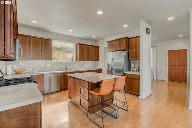 kitchen featuring light wood finished floors, backsplash, a breakfast bar, stainless steel appliances, and a sink