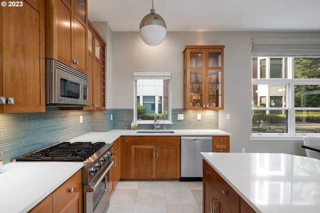 kitchen with appliances with stainless steel finishes, hanging light fixtures, light tile patterned flooring, backsplash, and sink