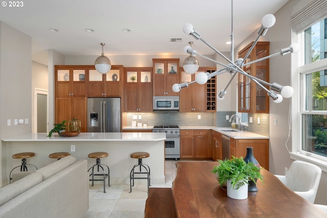 kitchen featuring appliances with stainless steel finishes, a kitchen breakfast bar, light tile patterned flooring, decorative light fixtures, and sink