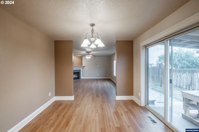 unfurnished dining area with ceiling fan with notable chandelier, a textured ceiling, and light wood-type flooring