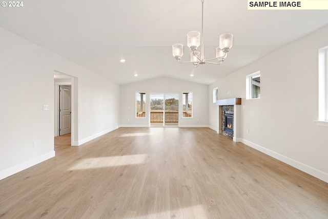 unfurnished living room featuring an inviting chandelier, lofted ceiling, a stone fireplace, and light wood-type flooring