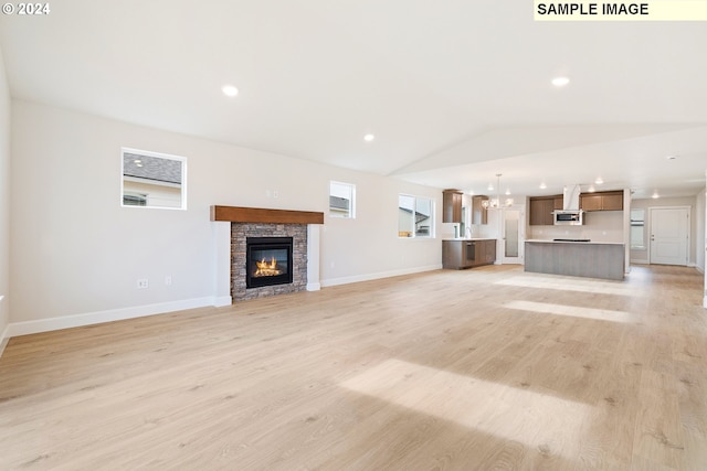 unfurnished living room with lofted ceiling, a stone fireplace, a chandelier, and light wood-type flooring