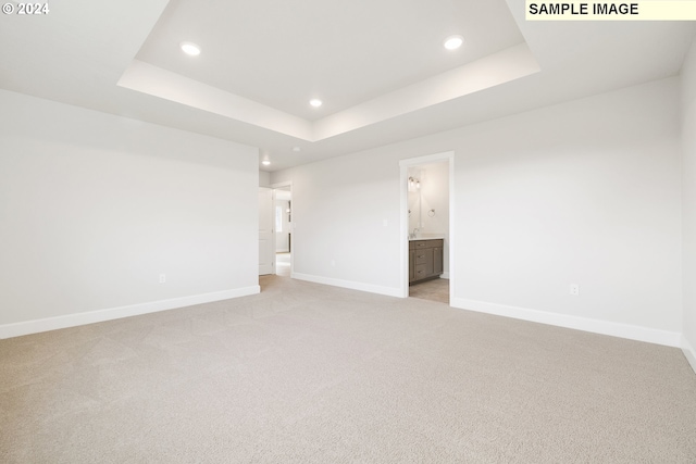 unfurnished bedroom with light colored carpet, a raised ceiling, and ensuite bath