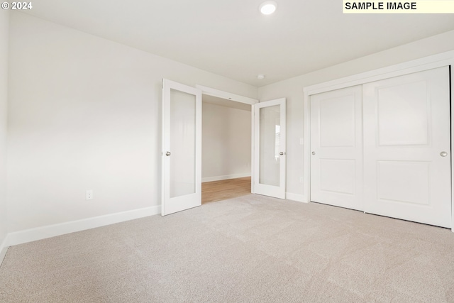 unfurnished bedroom with french doors, light carpet, and a closet